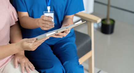 A woman in a blue uniform is sitting in a chair with a clipboard in front of her