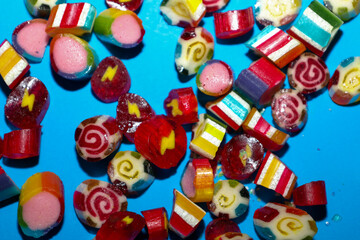 Obraz premium ​A bright scatter of small handmade caramel candies on a contrasting blue background. The lollipops are decorated with multicolored internal patterns in the shape of spirals, geometric stripes,