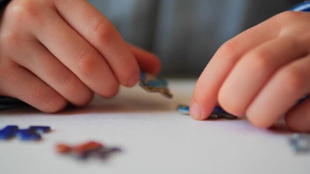 close-up of a child's fingers joining two interlocking jigsaw puzzle pieces on a white surface - Detailed view of a child solving a puzzle to illustrate problem-solving skills and fine motor developme