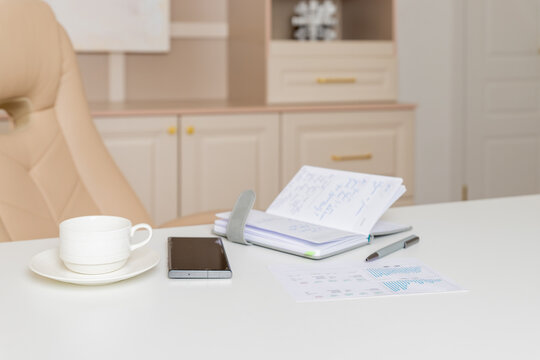 Office table with chairs,stationery, laptop. Office table desk with set of supplies.Work office,Business Concept.cup of hot coffee on white table with notebook, pen, beige armchair in meeting room.