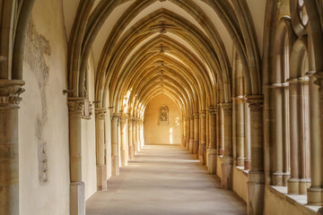 Obraz premium A long, narrow hallway in Gothic style with arched ceilings and a window. The arches are brown and the ceiling is white
