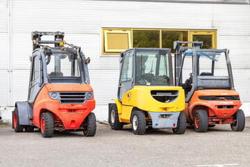 Colorful forklifts rest side by side in a quiet industrial yard on a sunny day