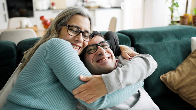 Mother and adult son smiling and embracing on a couch at home, showing a close family bond and support