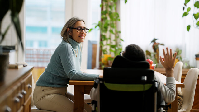 Woman and man with a disability talking at home. Man sitting in a wheelchair and gesturing, expressing ideas during conversation
