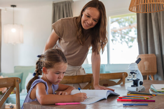 Mother supporting young daughter doing homework at home