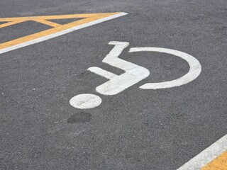 High-angle outdoor view of an accessible parking space on dark asphalt, marked with a white wheelchair symbol and bordered by yellow and white directional lines