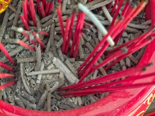 A top-down, close-up view of a red ceramic incense burner filled with grey ash and the remains of red joss sticks.