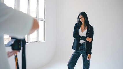 Professional photographer taking pictures of beautiful young female model posing in modern bright studio