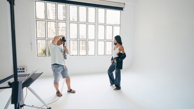 Photographer capturing stunning images of model posing in a professional studio, utilizing a laptop and softbox for optimal lighting