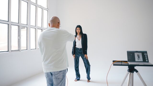Photographer capturing striking images of a model posing elegantly in a professional studio, utilizing tethered shooting with advanced technology