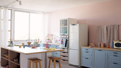 Bright kitchen interior featuring an island with stools, blue lower cabinets, a refrigerator, and a window with white curtains