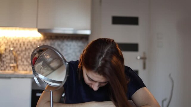 Young woman lowers her head in front of mirror giving up after long acne battle feeling drained hopeless and exhausted from constant skin problems at home