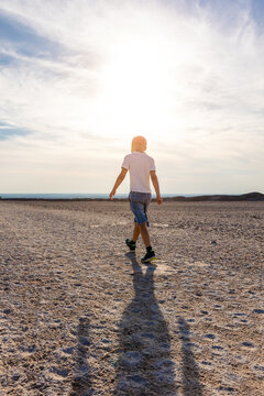 Back view child walking alone sandy dry solil toward horizon backlit sun silhouette express freedom independence calm journey. Natural stone landscape sunlight travel lifestyle childhood exploration