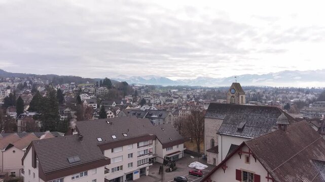 Drone flight over a traditional Swiss town with a historic church and clock tower at daytime.