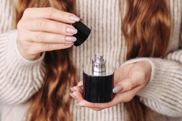 Fototapeta premium Woman holding perfume bottle in hands. Removing cap from fragrance container. Closeup of cosmetic product use. Female hands with beauty product. Daily personal care routine and luxury scent concept.