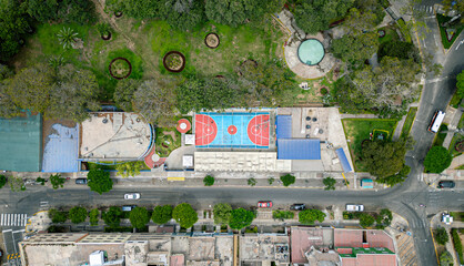 Aerial top down view of basketball court inside urban park next to city streets.