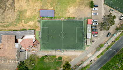 Green soccer field in use by players, top-down drone view.