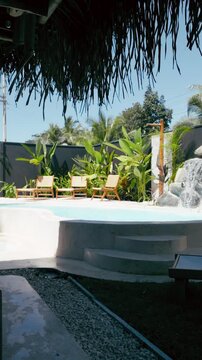 Exclusive tropical resort with a beautiful swimming pool, comfortable lounge chairs, and lush green plants on a sunny summer day. Vertical