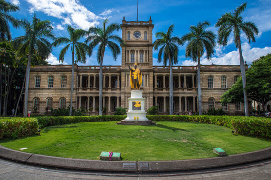 Honolulu, HI &mdash; November 29, 2024; The golden statue of King Kamehameha I standing before Aliʻiōlani Hale, framed by palms and bright tropical skies in Honolulu.