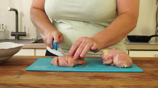 Woman cutting chicken fillet for cooking
