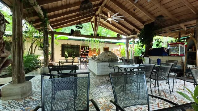 Empty outdoor patio of a tropical restaurant in costa rica featuring a wood fired pizza oven, patterned tile floor, and lush green plants