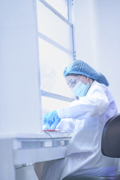 Professional surgeon working in sterile biosafety cabinet carefully. Female doctor preparing for operation in hospital laboratory. Female worker checking manufacturing standard in clean factory lab.