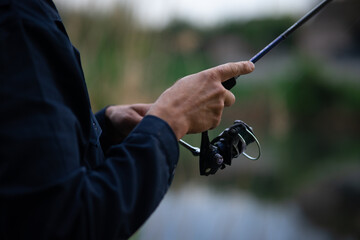 Close-up of a man's hand holding a spinning rod while fishing on the river, focus on the fishing tackle and grip.