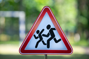 Triangular warning road sign "Children" featuring silhouettes of two kids on a solid green background.
