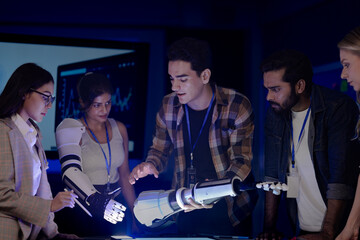 Robotics engineers in an RD lab test an AI powered prosthetic arm. The diverse team, including an Indian woman, analyzes the bionic prototype's hardware and design at night.