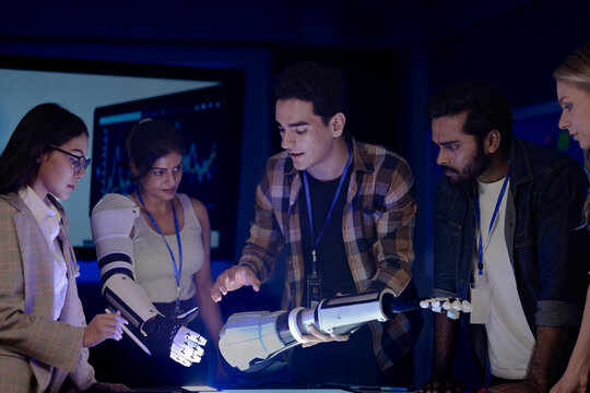 Robotics engineers in an RD lab test an AI powered prosthetic arm. The diverse team, including an Indian woman, analyzes the bionic prototype's hardware and design at night.