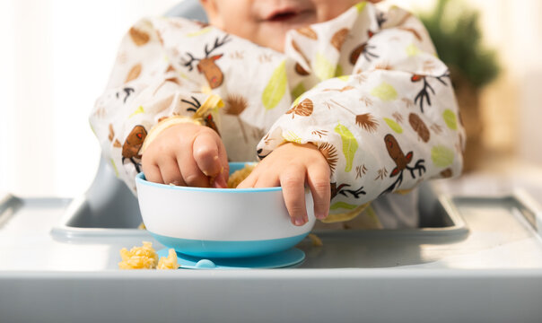 Baby led weaning infant eating messy meal in high chair