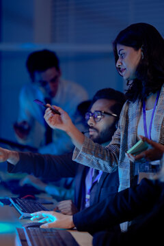 Dedicated support team working late night shift in blue light office. Male employee with headphones monitoring data on computer screen for cyber security work.