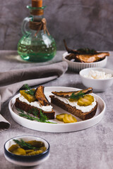 Sandwiches with ricotta, pickles and sprats on rye bread on a plate on a table vertical view