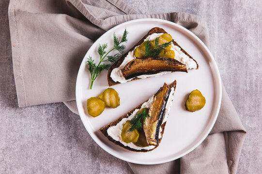 Close up of sandwiches with ricotta, pickles and sprats on rye bread on a plate on a table top view