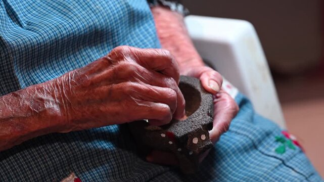 Close-up of elderly hands using a traditional Mexican molcajete, detail of aged skin with sunspots and wrinkles on elderly hands