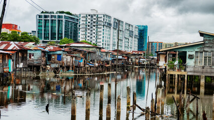 Fototapeta premium Kota Kinabalu, Malaysia. Illegal Filipino immigrants Bajau live in pile-buildings settlement, slum. Some houses been demolished, residents evicted. Modern high-rise buildings stand in background