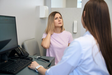 Young woman touching her neck and having consultation with her doctor