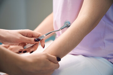 Doctor neurologist inspecting female hand nervous system with nerve wheel