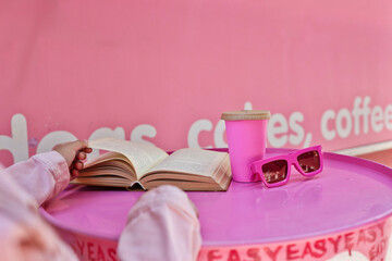 Enjoying a book and coffee on a vibrant pink table with sunglasses