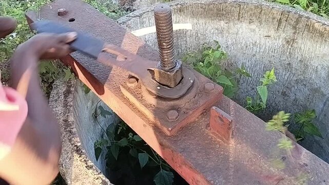 A hardworking differently-abled person with an amputated arm operating a rusty sluice gate mechanism at a lake, demonstrating resilience and strength.