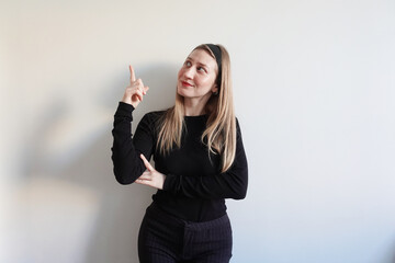 Młoda kobieta wskazuje palcem w górę, stojąc pewnie z ręką na biodrze. Koncepcja pewności siebie i prezentacji pomysłu. © Izabela