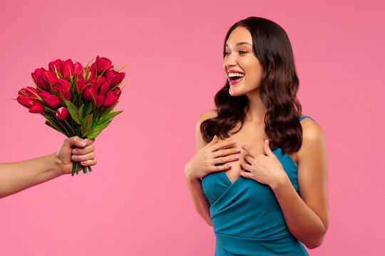 Beautiful surprised woman receiving bouquet of tulips on pink studio background. International Women's Day celebration