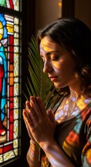 Fototapeta premium Woman praying with palm branch by stained glass window. Spiritual moment for worship and contemplation during Palm Sunday or Easter.