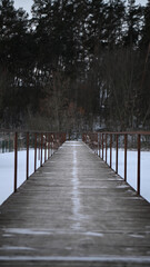 Obraz premium Wooden path leads through snow to trees under cloudy sky in winter landscape