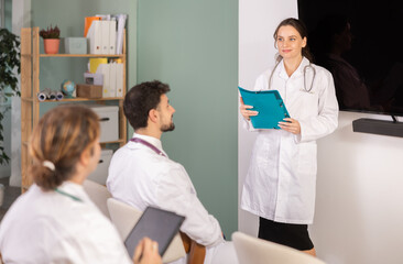 Fototapeta premium Female medical speaker gives lecture, uses paper document presentation materials shorthand dictation. Professional meeting, medical council