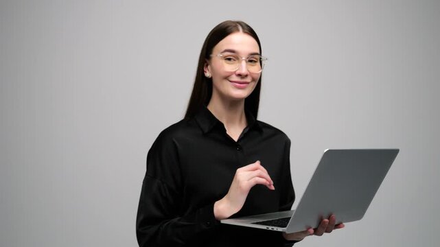 Woman holds laptop and smiles in a simple studio background