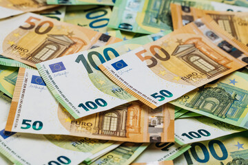 Obraz premium Close-up view of assorted Euro banknotes including 50 and 100 denominations scattered on a flat surface, showcasing detailed designs and colors