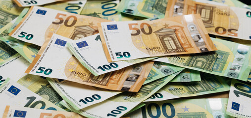 Obraz premium Close-up view of assorted Euro banknotes including 50 and 100 denominations spread out on a flat surface, showcasing detailed designs and colors