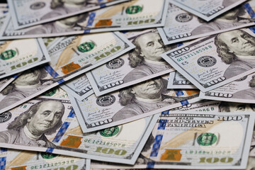 Stacks of hundred-dollar bills spread out on a flat surface, showcasing intricate details of the currency design and various denominations visible in the arrangement