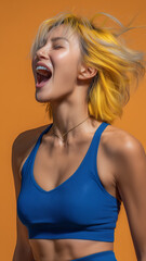 Dynamic portrait of a joyful athletic woman with yellow-blonde hair shouting in excitement against a bright orange background